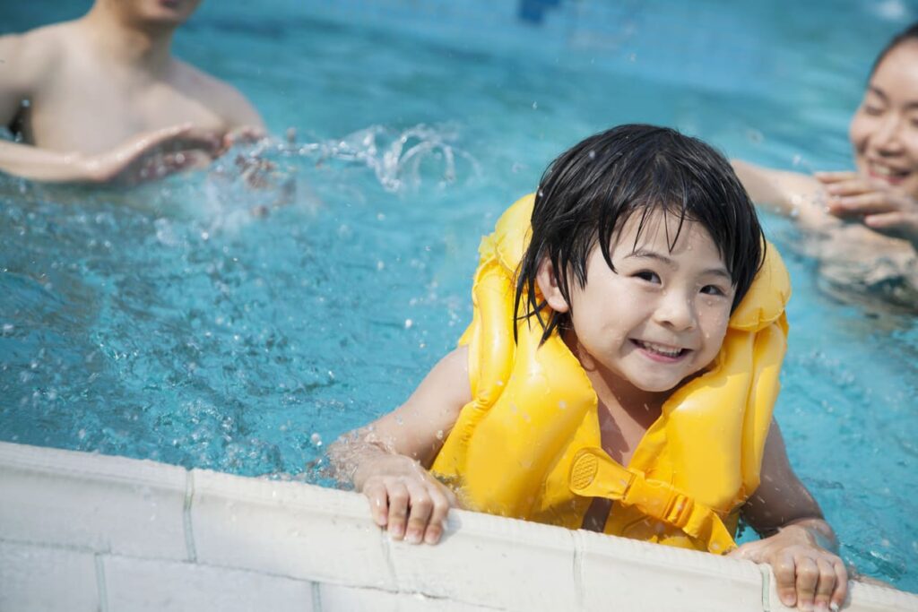 Smiling toddler swims in the pool while wearing a yellow life jacket.