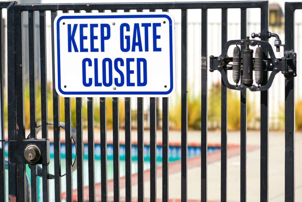 A blue and white sign on a black pool gate reads “Keep Gate Closed."