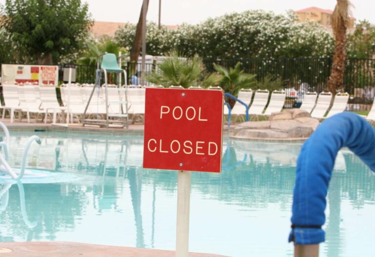 : A square red sign reading “Pool Closed” stands in front of an empty pool