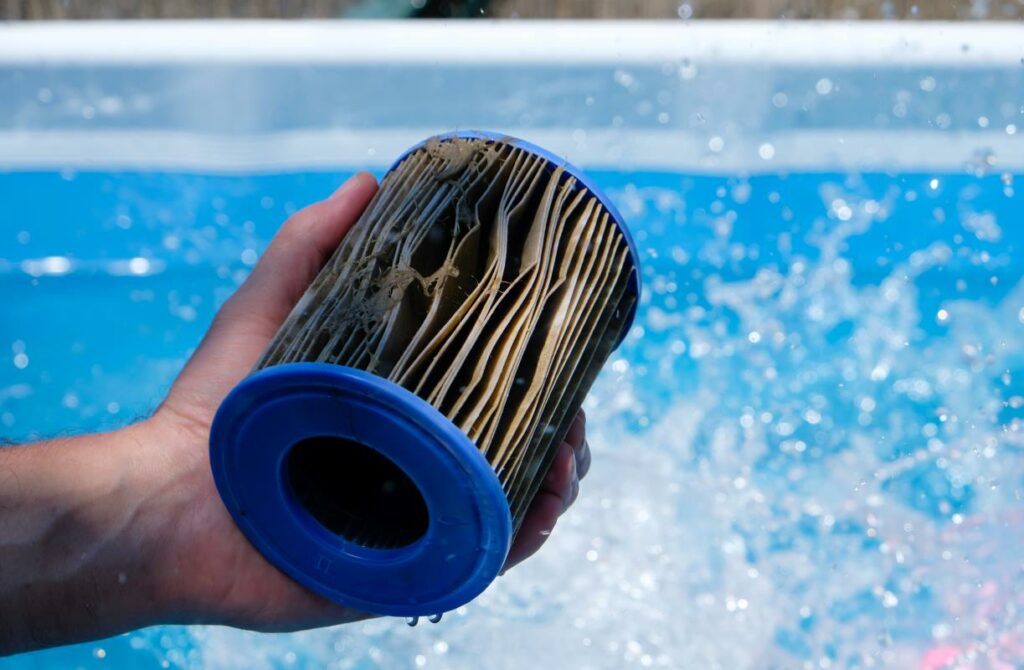 Dirty pool filter cartridge in a man’s hand on water splash background. 