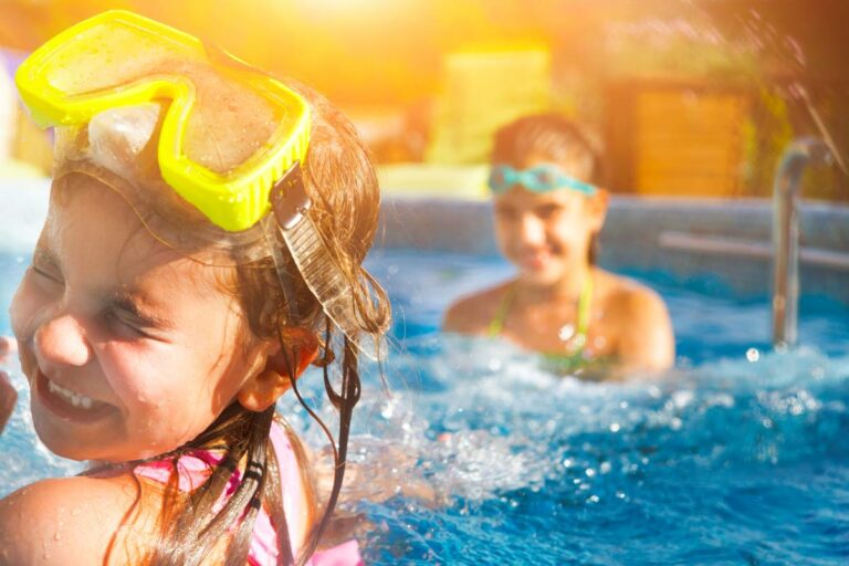 Two children playing in the pool during the summer with goggles on.