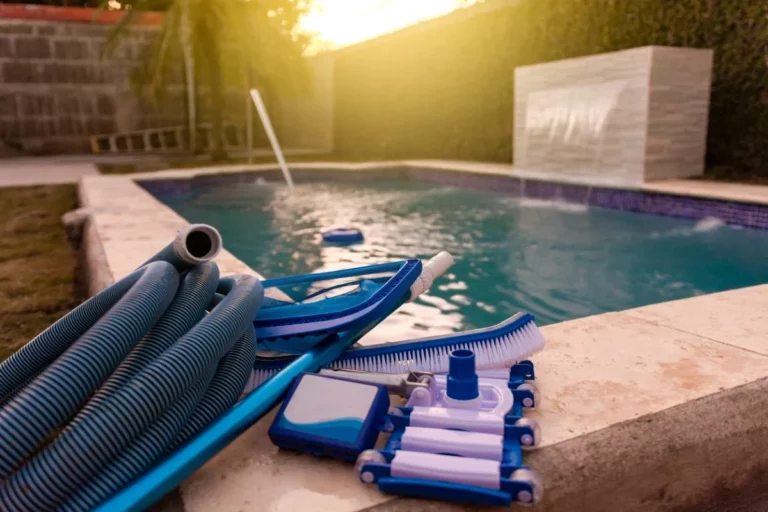 A swimming pool in the background with a pool cleaning and maintenance set sitting on the corner, complete with a vacuum cleaner, pH testing kit, leaf picker, and pool sweeper.