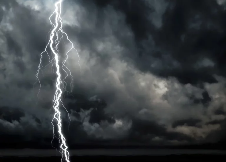 A dark and cloudy sky is behind a vibrant lightning strike.