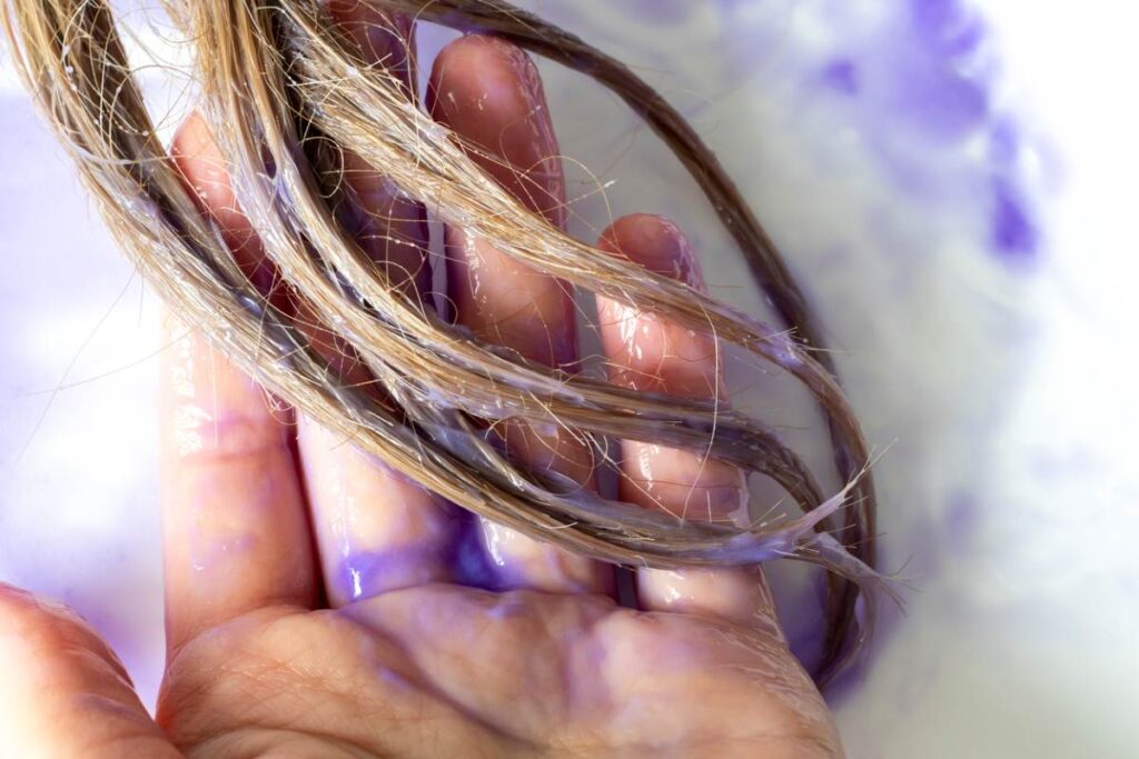 A person applies a purple hair mask to blonde hair.